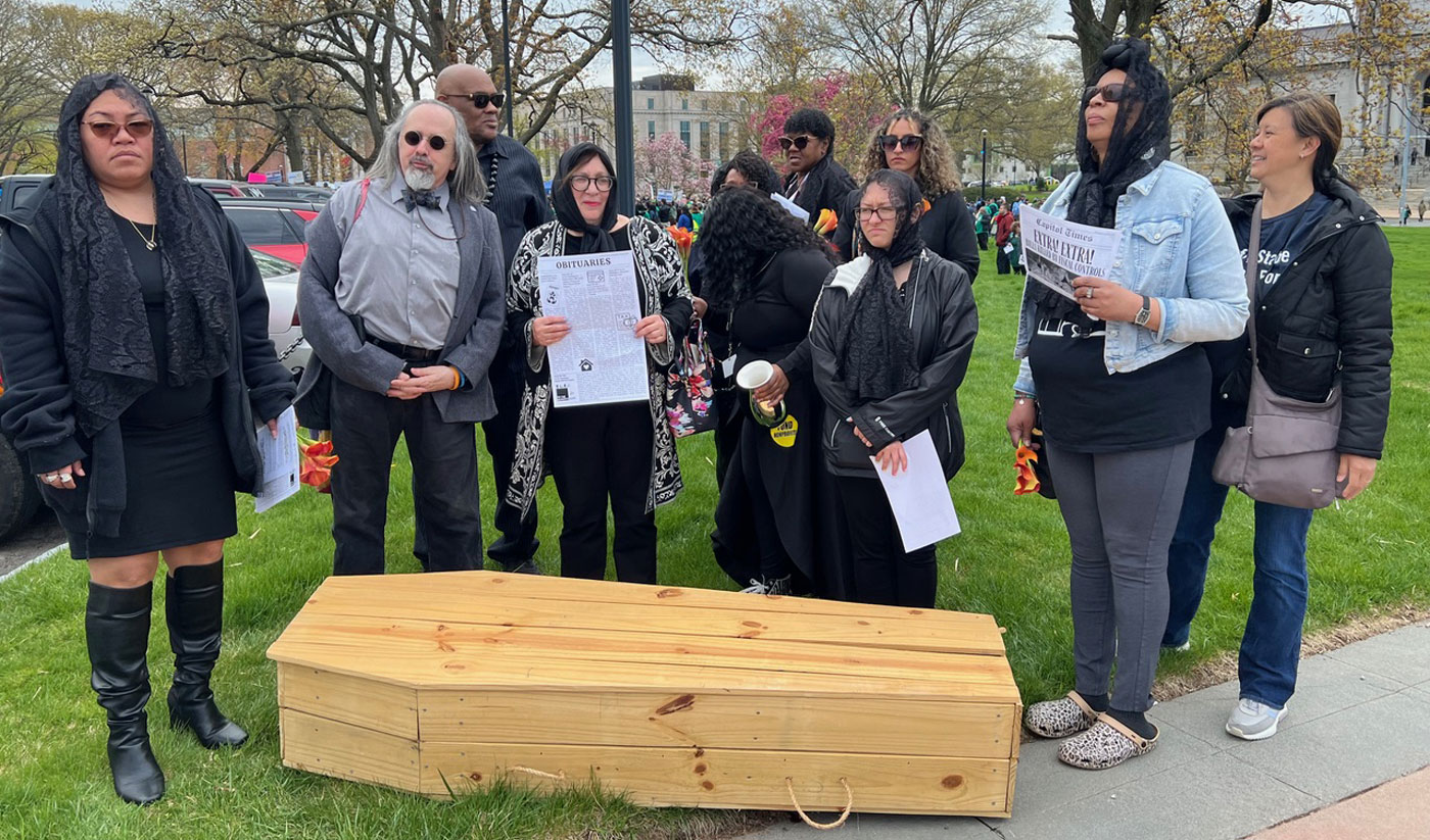 Protestors on the green with signs in front of a coffin
